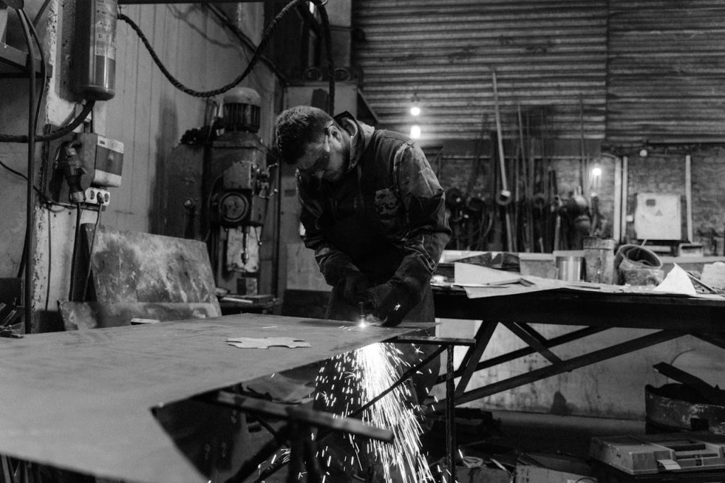 A skilled worker welding metal in an industrial factory setting, in black and white.